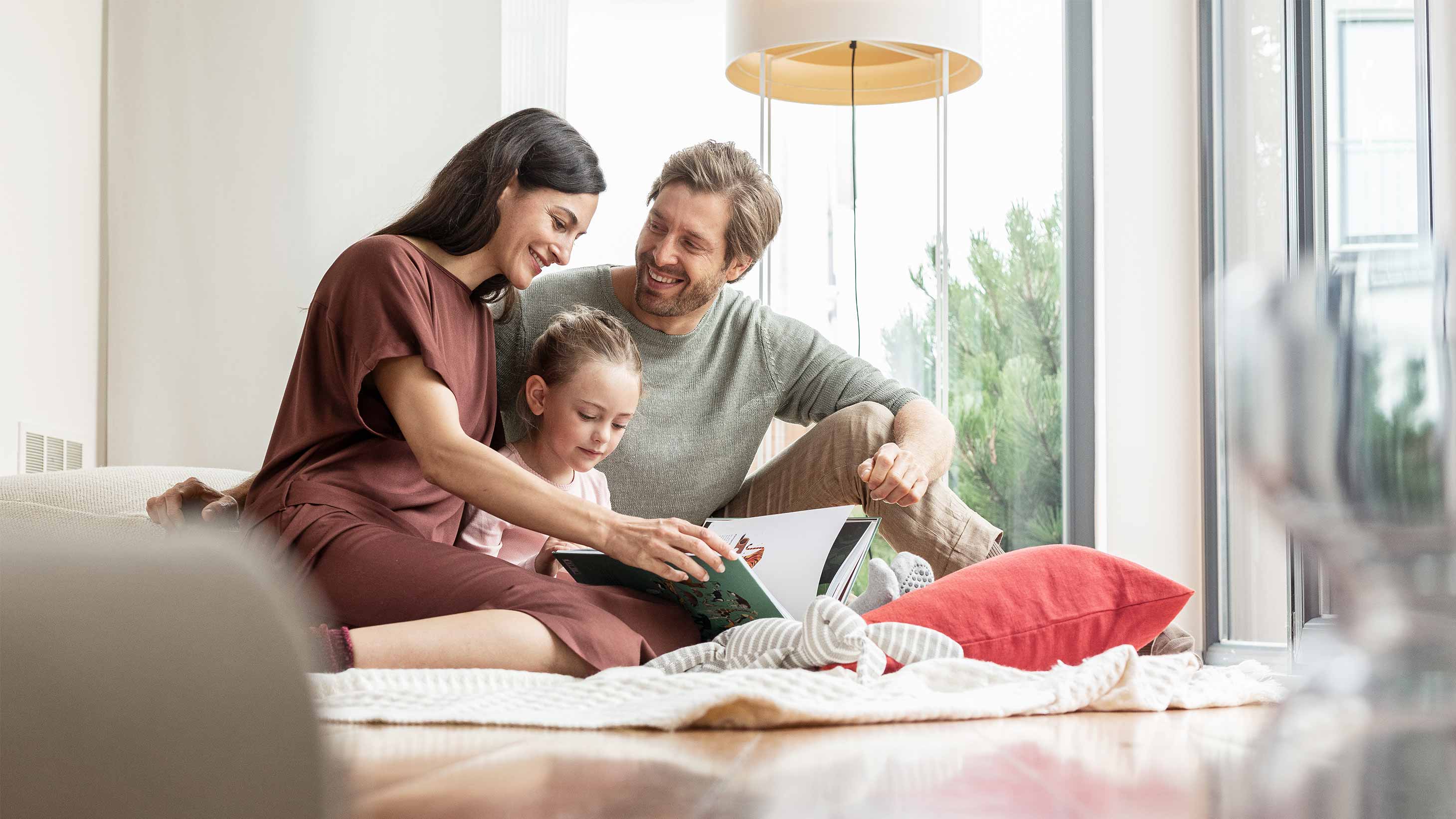 Eine Familie sitzt auf dem Boden und schaut in ein Buch.