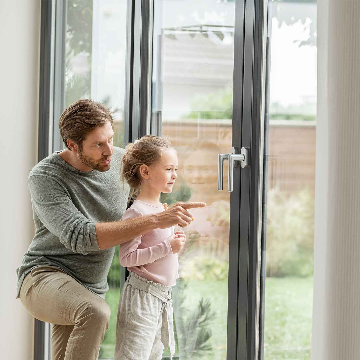 Vater und Tochter stehen vor dem Fenster und schauen hinaus in den Garten